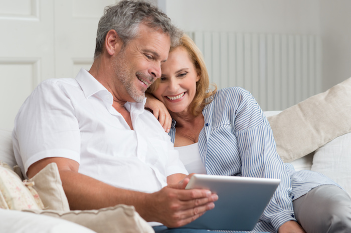 Happy Mature Couple Sitting On Sofa With Digital Tablet